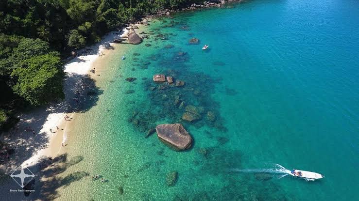Ilha das Couves vista de cima, com praia, pedras e uma lancha chegando